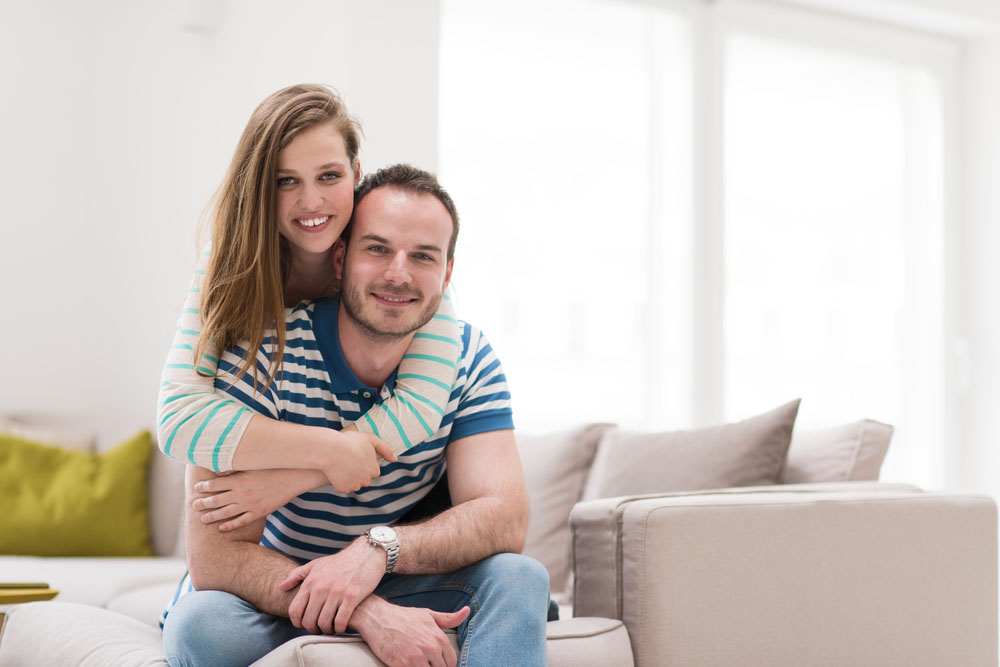 Prestige Wealth Partners - loving couple sitting on a sofa smiling at the camera